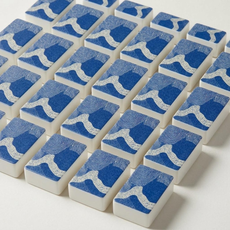 American mahjong tile set with custom blue and white coral and shell print backs, fanned out to show front faces and matching backs — a complete mah jongg tile set built for serious play, included with a coordinating coastal mahjong mat, card holders, and tile bag.