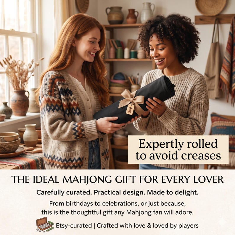 Op de afbeelding: Twee mensen houden een opgerold zwart item vast, vastgebonden met een lint en een label. De tekst luidt "Expertly rolled to avoid creases" en "THE IDEAL MAHJONG GIFT FOR EVERY LOVER". De afbeelding suggereert een cadeau voor Mahjong-liefhebbers.