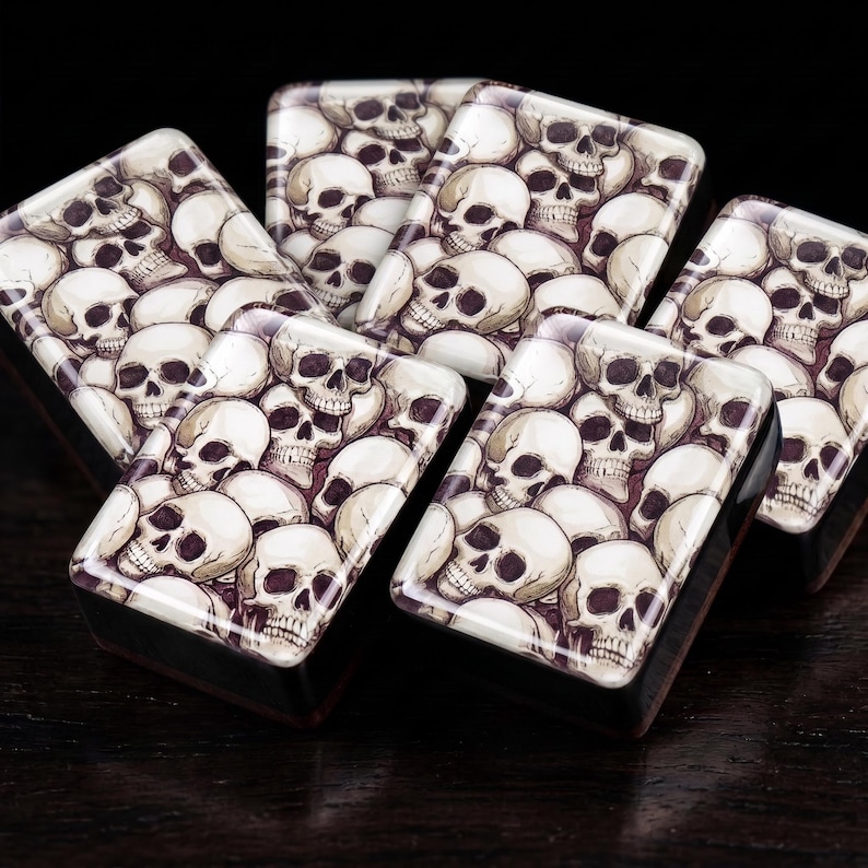Close-up of six glossy Halloween mahjong tiles with a stacked ivory and charcoal gothic skull design, arranged on a dark wood table.