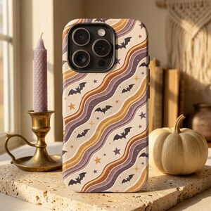May include: A smartphone case featuring a repeating pattern of diagonal wavy lines in shades of cream, tan, and muted purple. The design is decorated with small black bat silhouettes and various sizes of gold and purple stars scattered throughout.