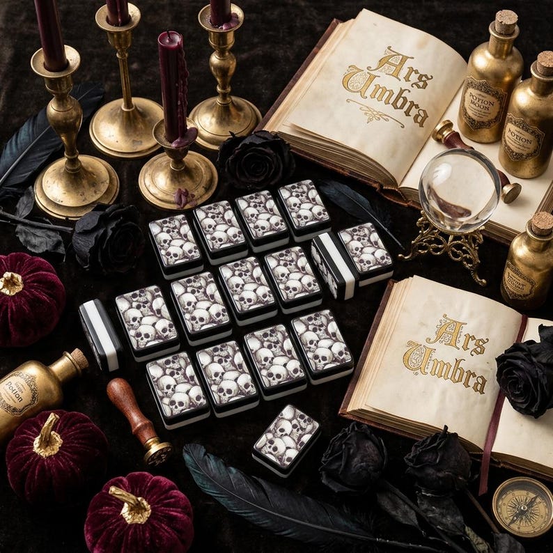 Gothic skull mahjong tiles displayed on a black tablecloth with candles and dark florals for a moody Halloween game night setup.