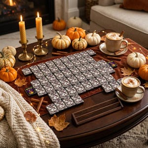 Overhead view of a complete Halloween mahjong tile set with ivory and charcoal gothic skull artwork, arranged in rows on a dark wood surface.