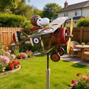 May include: A metal garden sculpture of Snoopy as a World War I flying ace in a biplane. The biplane is olive green with red, white, and blue accents. Snoopy wears a brown aviator helmet and a red scarf. The biplane has the number B7270.