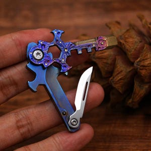 May include: A multi-tool with a blue and purple finish, featuring a key-shaped design with a bottle opener, knife, and other tools. The tool has a metallic finish with gold accents and a small silver blade.