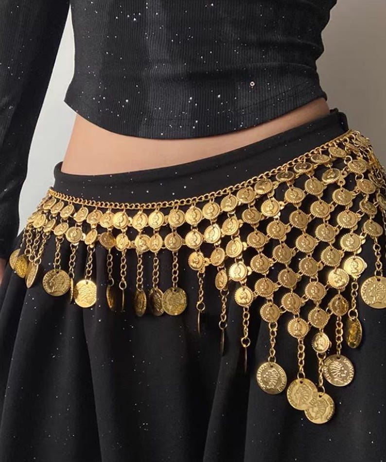 Pode incluir: Um cinto de dan&ccedil;a do ventre dourado com detalhes de moedas e correntes. O cinto &eacute; usado sobre uma saia preta e apresenta fileiras de moedas circulares com correntes e moedas penduradas. &Eacute; um acess&oacute;rio decorativo.