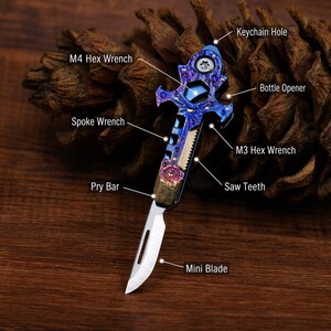 May include: A multi-tool knife with a blue and purple handle, featuring a mini blade, saw teeth, and a bottle opener. It also includes an M4 and M3 hex wrench, a spoke wrench, and a pry bar. A keychain hole is visible at the top.