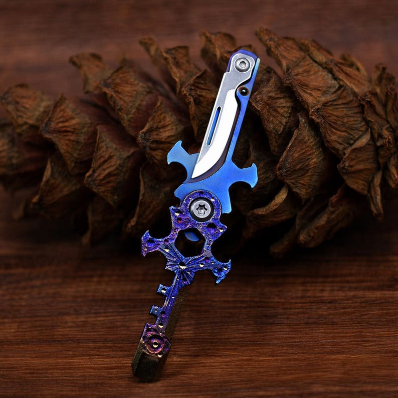May include: A decorative knife with a blue and silver blade and handle. The handle features an ornate, stylized design with purple accents. The knife is set against a brown, textured background, suggesting a natural setting.