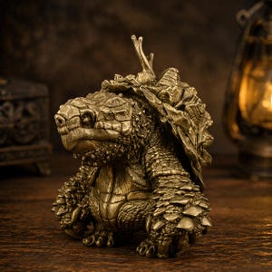 Könnte beinhalten: Eine detaillierte, bronzefarbene Schildkrötenfigur mit strukturierter Schale und aufwendigen Details. Die Skulptur zeigt eine realistische Darstellung des Kopfes, der Beine und des Panzers einer Schildkröte, mit einem kleinen pflanzenartigen Element auf dem Rücken. Die Figur steht auf einer Holzoberfläche.