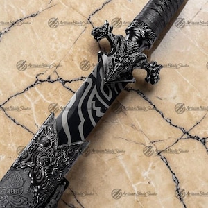 May include: A detailed close-up of a black and silver decorative sword. The blade features a unique pattern, and the hilt is adorned with dragon motifs. The scabbard and handle are wrapped in black material, showcasing intricate designs.