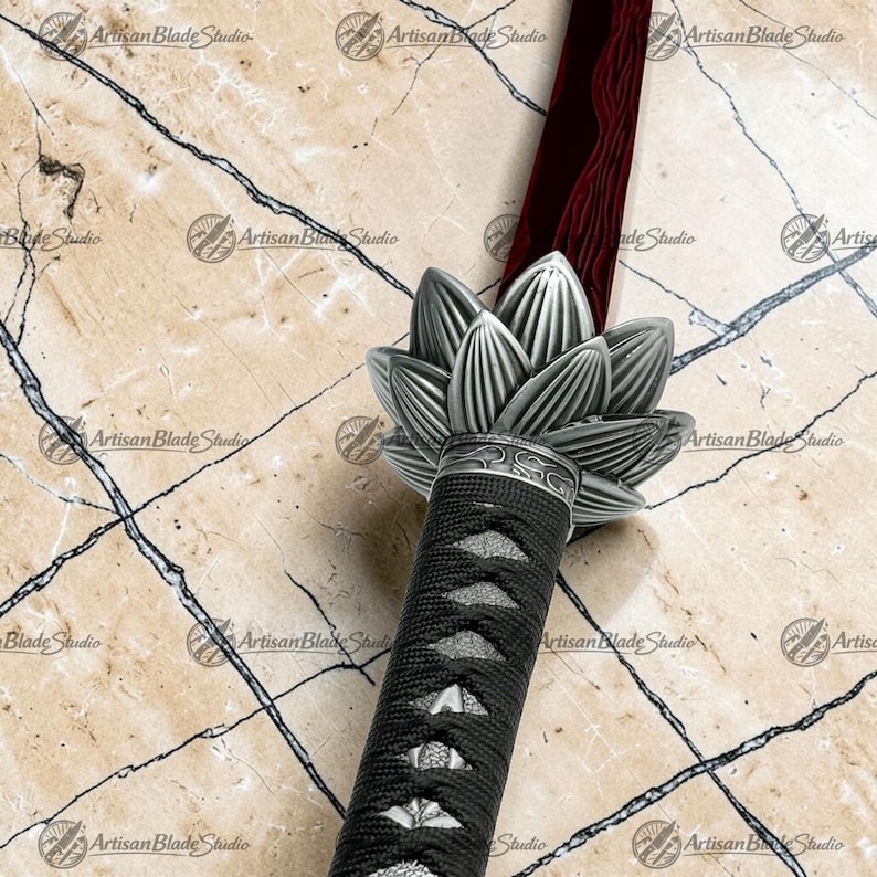 May include: A sword with a deep red blade featuring a wavy pattern, a silver metal handguard shaped like a blooming lotus flower, and a black cord-wrapped handle with a textured underlay, all displayed against a light marble background.