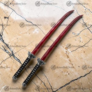May include: Two swords with deep red blades featuring a wavy hamon line pattern. Each sword has a black handle with a silver-toned lotus-shaped tsuba guard. The blades are long and curved, extending from the ornate metal hilts to sharp points.