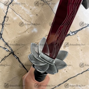 May include: A sword featuring a deep red blade with a subtle wavy pattern and a silver-colored tsuba shaped like a multi-petaled flower. The handle is wrapped in black cord, providing a textured grip for the hilt of this decorative bladed weapon.