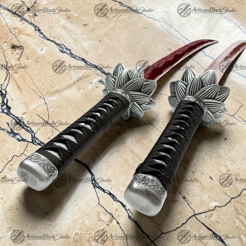 May include: Two daggers with curved, deep red blades and black cord-wrapped handles. Each handle features a silver-toned metal pommel and a silver-toned metal guard shaped like a multi-petaled flower. The blades have a visible wavy temper line.