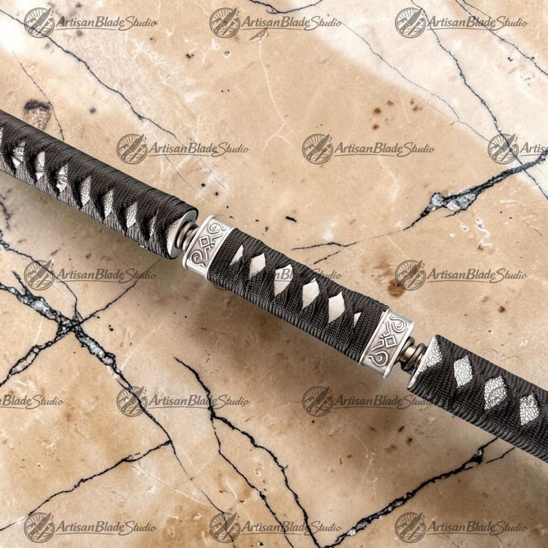 May include: A sword handle featuring a black cord-wrapped grip with diamond-shaped white underlay patterns. The handle is divided into three sections by two silver-colored metal collars, each engraved with intricate geometric line designs.