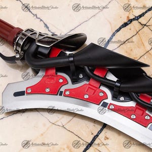 May include: Detailed view of a custom sword with a red handle and accents. The blade is silver with red and black detailing. The sword has a complex design with metal and plastic components. The words "Artisan Blade Studio" are visible.