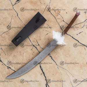 May include: A handcrafted sword with a textured blade and a brown handle. The sword features a white feather accent near the blade and a black sheath. The blade has a unique pattern. The sword is displayed on a marble-like surface.