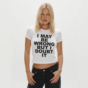 Op de afbeelding: Witte crop top met de zwarte tekst "I MAY BE WRONG BUT I DOUBT IT". Het model draagt een zwarte jeans. De top is een casual kledingstuk voor dagelijks gebruik, tegen een witte achtergrond.