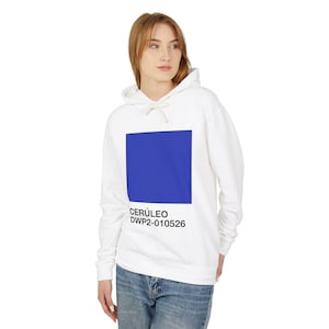 Pode incluir: Moletom branco com um grande quadrado azul cerúleo na frente. Abaixo do quadrado azul está o texto "CERÚLEO DWP2-010526" em preto. O moletom tem cordão e capuz.