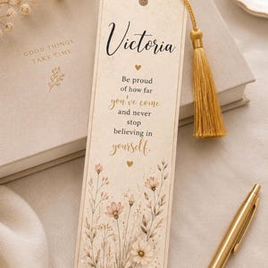 Könnte beinhalten: Ein rechteckiges Lesezeichen aus Papier mit cremefarbenem Hintergrund, das den Namen Victoria in schwarzer Schreibschrift zeigt, gefolgt von dem Text Be proud of how far you've come and never stop believing in yourself. Es hat eine goldene Quaste.