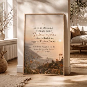 May include: A framed print with a light wood frame. The print features a soft, warm-toned landscape with text in German. The text reads "Es ist in Ordnung, wenn du deine Seelenmenschen außerhalb deines engsten Kreises findest."