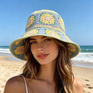 May include: A crocheted bucket hat with a floral design. The hat features a light blue base with yellow and pink flower motifs. The brim and edges are trimmed in green. The hat is worn on a person at the beach.