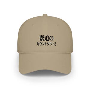 Peut inclure: Casquette de baseball beige avec une visière incurvée. Le chapeau porte du texte japonais noir sur le devant. Le texte se lit "Compte à rebours !" en japonais. La casquette est en matière souple et a une couronne structurée.