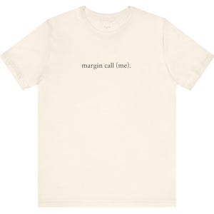 May include: Cream-colored t-shirt with the phrase "margin call (me)." printed in black, centered on the front. The shirt has short sleeves and a crew neck. The fabric appears to be a soft, lightweight material.