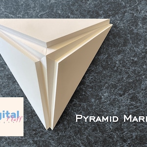 Puede incluir: Un objeto blanco en forma de pirámide hecho de tres capas de cartón. El objeto está sobre un fondo gris oscuro con un texto blanco superpuesto que dice "PYRAMID MARK II".