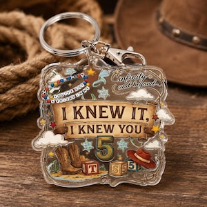 May include: A clear acrylic keychain featuring a western-themed design with a brown scroll banner reading I KNEW IT, I KNEW YOU. The graphic includes cowboy boots, a brown hat, alphabet blocks, the number 5, and text reading infinity and beyond.