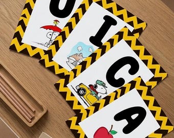 Può includere: Quattro cartoncini rettangolari con un bordo a zig-zag giallo e marrone. Ogni cartoncino presenta una grande lettera nera che compone la parola UICA e un'illustrazione dei Peanuts. Il primo mostra Snoopy con un ombrello rosso, il secondo un personaggio, il terzo Snoopy in un'auto gialla e il quarto una mela rossa.