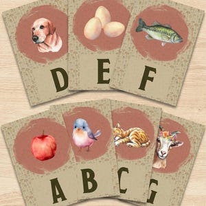 May include: A set of seven rectangular educational cards featuring a beige background with a mushroom pattern. Each card displays a letter from A to G in dark brown, paired with a watercolor illustration of a dog, eggs, fish, apple, bird, cat, or goat.