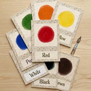 May include: A collection of color cards with watercolor circles in various hues, including red, yellow, and blue. Each card has the color name printed on it. A paintbrush is also visible.