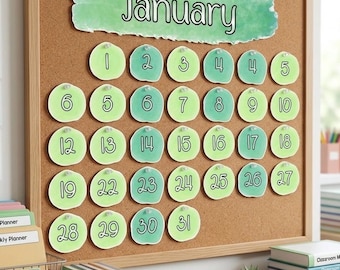 Può includere: Una bacheca in sughero con cornice in legno chiaro mostra un calendario per gennaio. Il nome del mese è scritto in nero su un'intestazione verde in stile acquerello. Trentuno ritagli di carta circolari verdi con numeri neri sono appuntati.