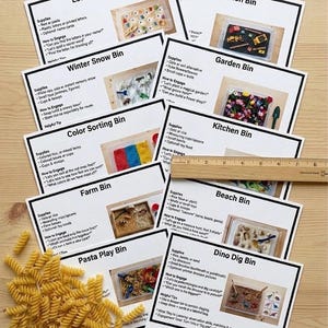 May include: A collection of educational activity cards for children, featuring various themes like a letter search bin, construction bin, and color sorting bin. The cards are arranged on a wooden surface, with a pile of pasta and a ruler visible.