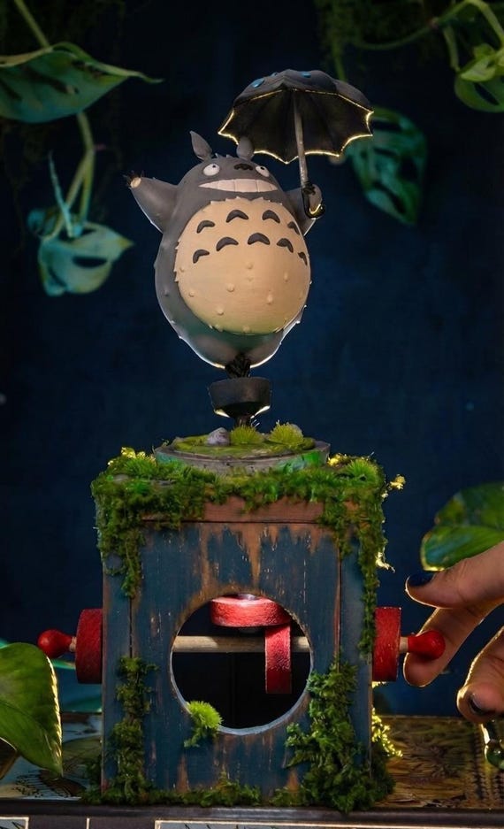 A handcrafted wooden automaton where a 3D-printed Totoro figure actually moves via a mechanical cam mechanism synced to a music box — Studio Ghibli magic made physical.