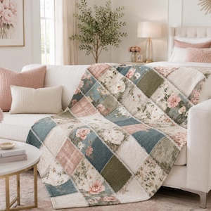 May include: A patchwork quilt featuring a variety of square fabric panels in shades of sage green, dusty blue, cream, and soft pink. The design includes floral patterns, solid textured squares, and plaid prints with frayed edges between each section.