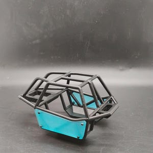 Puede incluir: Un marco de jaula antivuelco tubular negro para un vehículo a control remoto, con una estructura de metal negro mate y paneles laterales de color azul cian brillante sujetos con tornillos pequeños. El diseño abierto incluye un techo.