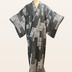 May include: A full-length kimono featuring a monochromatic patchwork design in shades of black, gray, and white. The garment displays a repeating geometric pattern of rectangular blocks, each filled with intricate, varied floral and abstract motifs.