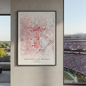 May include: A framed map print of the University of Georgia in Athens, GA, with a red and white color scheme. The map details the city's layout, with the university's name and coordinates at the bottom. The print is displayed in a modern interior setting.