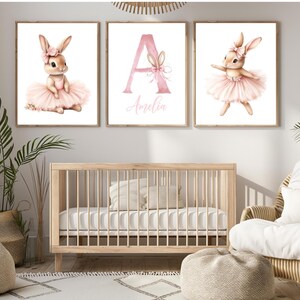 May include: Three wall art prints featuring watercolor illustrations of a bunny wearing a pink tutu and bow. The center print displays a large pink letter A with the name Amelia written below it in a script font on a white background.