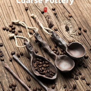 Puede incluir: Cucharas de cerámica gruesa prensadas a mano con granos de café sobre una superficie de madera. Las cucharas son de color marrón oscuro y tienen un aspecto rústico y texturizado. Incluye el texto "Hand-pressed Coarse Pottery".