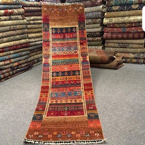 May include: A long, rectangular runner rug featuring a vibrant, multi-colored geometric and animal pattern in shades of red, orange, blue, and brown. The rug displays the text 8254 and 297x82 in the upper right corner, with fringe at the ends.