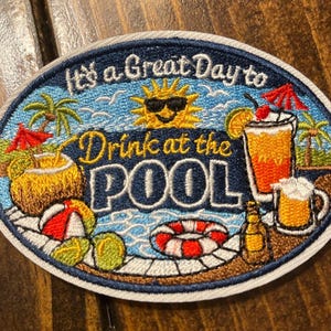 May include: An oval embroidered patch featuring a blue pool scene with a yellow sun wearing sunglasses, palm trees, a beach ball, and a life preserver. The text reads It's a Great Day to Drink at the POOL, surrounded by tropical drinks.