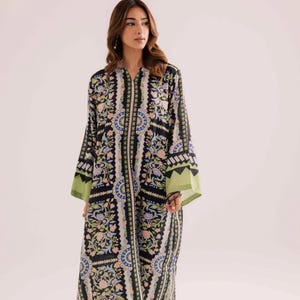 May include: A long, flowing dress with a black background and a floral pattern in shades of pink, blue, and green. The dress has long sleeves with green cuffs and a matching green hemline. The dress is worn by a person.