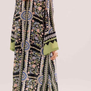 May include: A long, flowing dress with a black background and a floral pattern in shades of pink, blue, and green. The dress has long sleeves with green cuffs and a split up the side. The model is wearing high-heeled shoes.