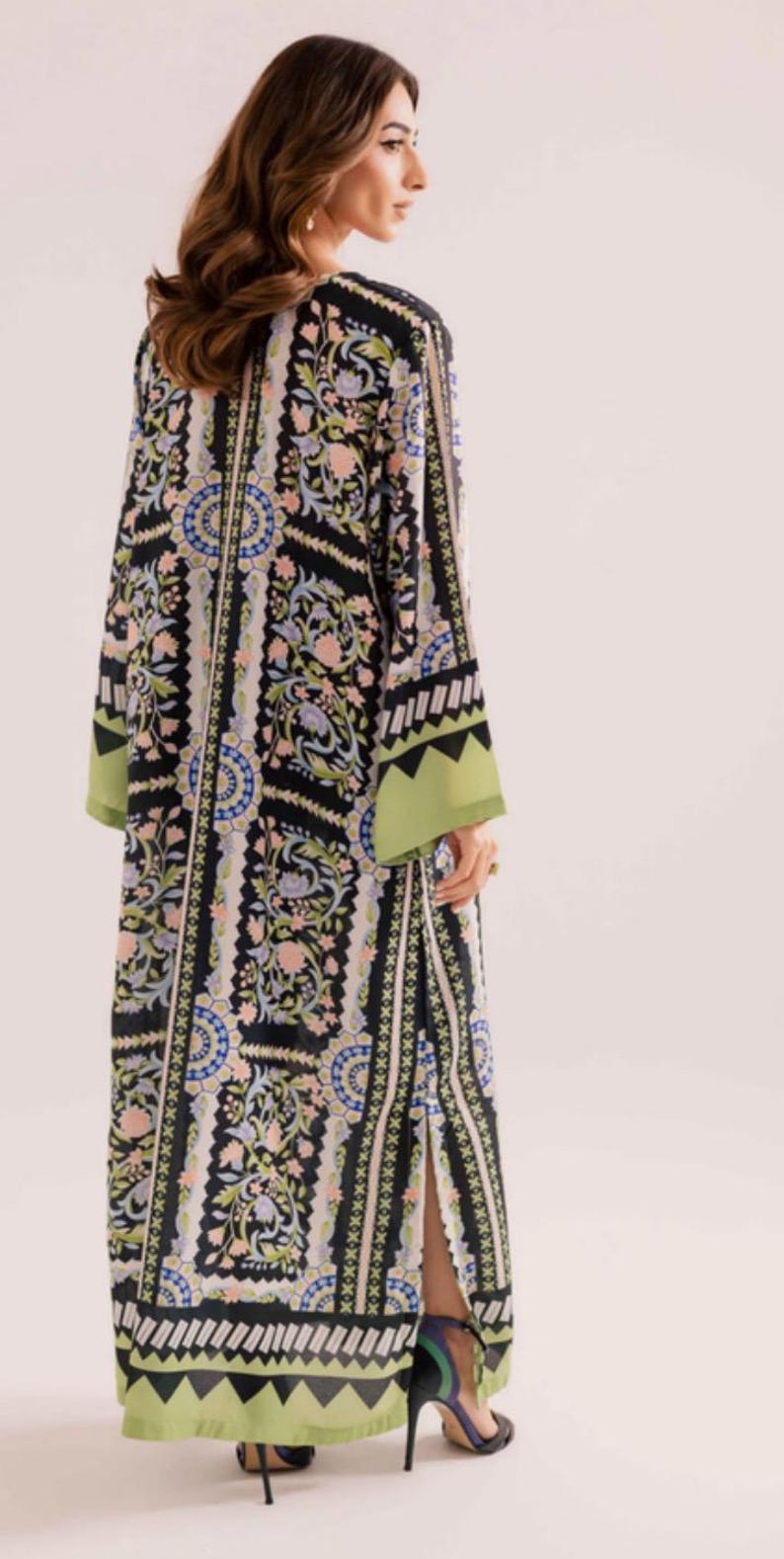 May include: A long, flowing dress with a black background and a floral pattern in shades of pink, blue, and green. The dress has long sleeves with green cuffs and a split up the side. The model is wearing high-heeled shoes.