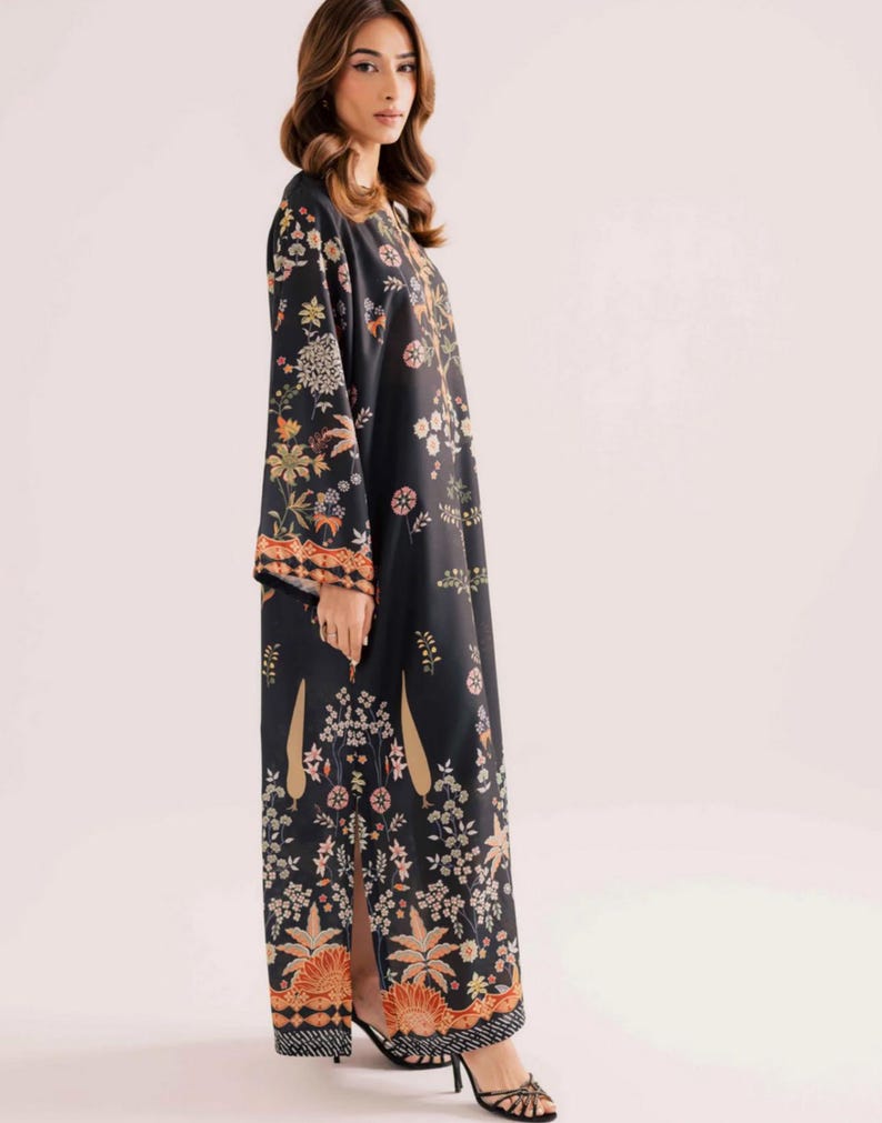 May include: A long, black dress with a floral pattern in shades of orange, yellow, and green. The dress has long sleeves and a slit up the side. The hemline and sleeve cuffs have a patterned border.