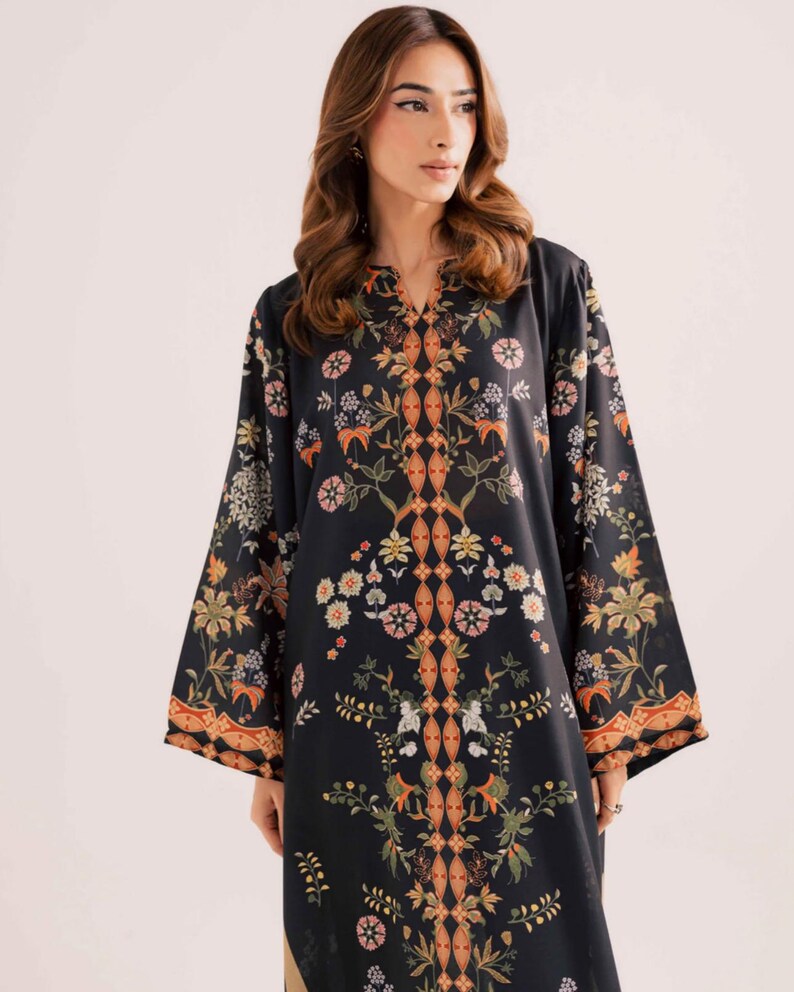 May include: Black tunic with a V-neck and long sleeves. The tunic features a floral pattern in shades of orange, green, and white. The floral design is symmetrical and covers the front and sleeves of the tunic. The tunic is made of a soft, flowing fabric.