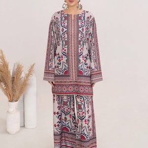 May include: A two-piece outfit featuring a long-sleeved tunic and matching pants. The ensemble is primarily light beige with a detailed pattern in red, blue, and green. The tunic has a split neckline, and the pants have a drawstring waist. The outfit is worn with sandals.