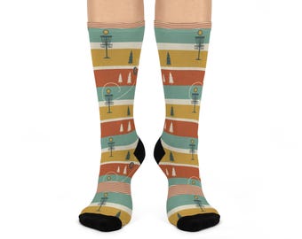 May include: Knee-high socks with a repeating pattern of disc golf baskets, trees, and flying discs. The socks feature horizontal stripes in teal, orange, yellow, and red. The heels and toes are black.